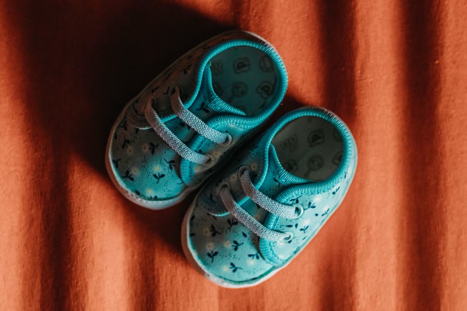 Sepatu bayi rajut warna biru langit di atas kain terakota